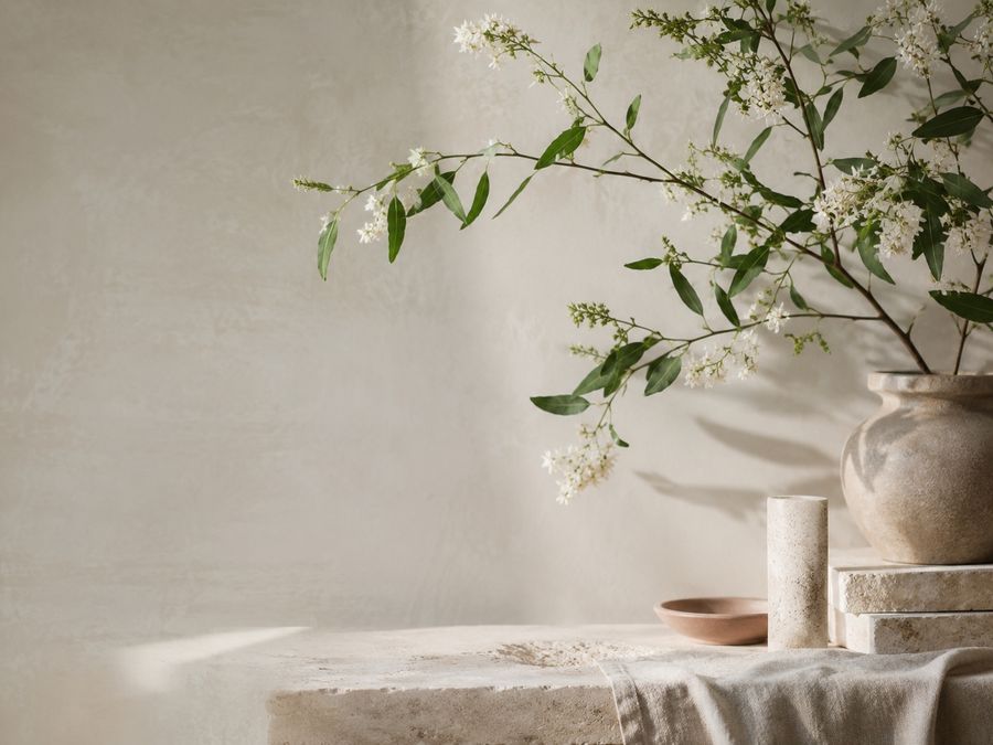Flowering branches in a stone vessel against a pale plaster wall.